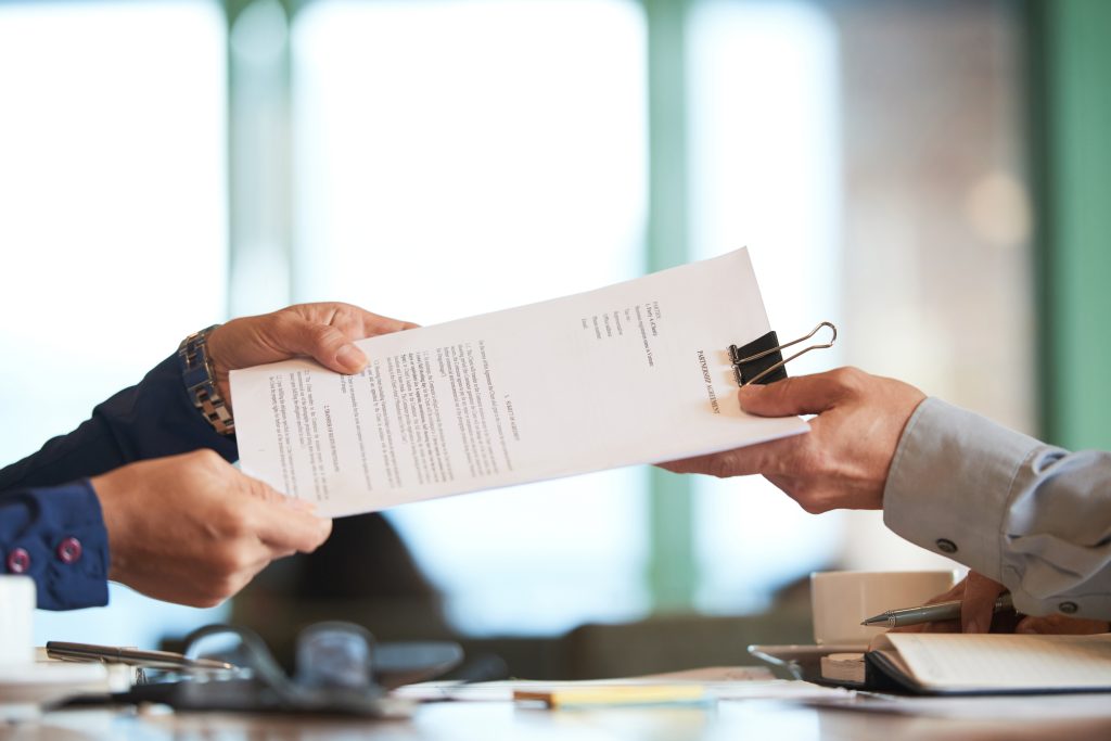 Hands passing a contract across a desk