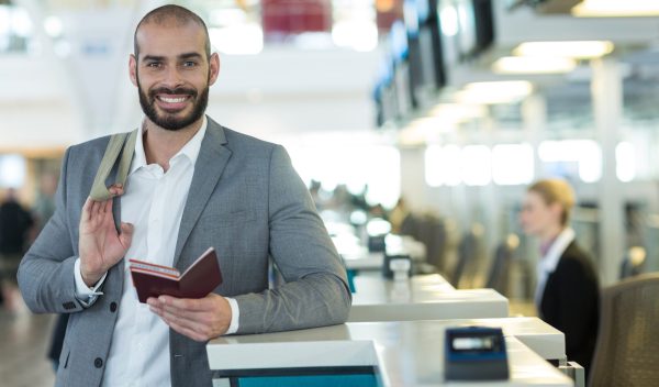 Portrait of smiling businessman standing at check-in counter with passport and boarding pass at airport terminal
